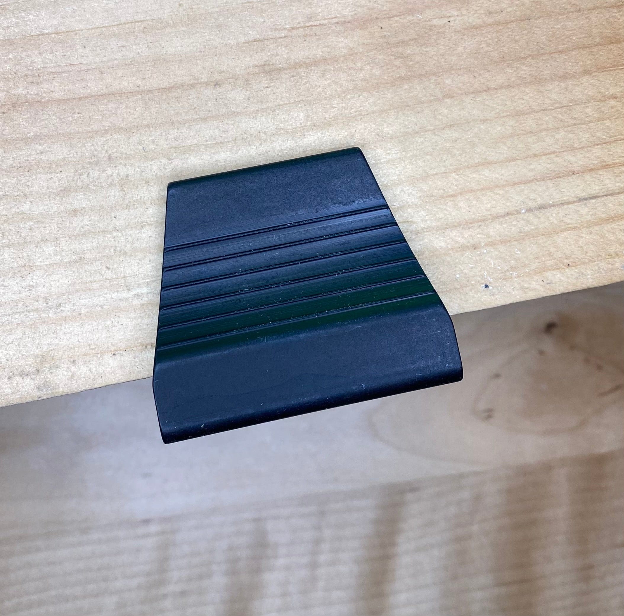 A VERITAS DOVETAIL SADDLE MARKER from the brand VER, made of black plastic and featuring ridges similar to a precision-machined tool, rests on a wooden surface.