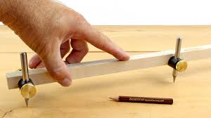 A hand adjusts VER Beam Compass Heads, a classic tool for drawing large circles or arcs on wood. A pencil rests nearby on the light-colored tabletop.