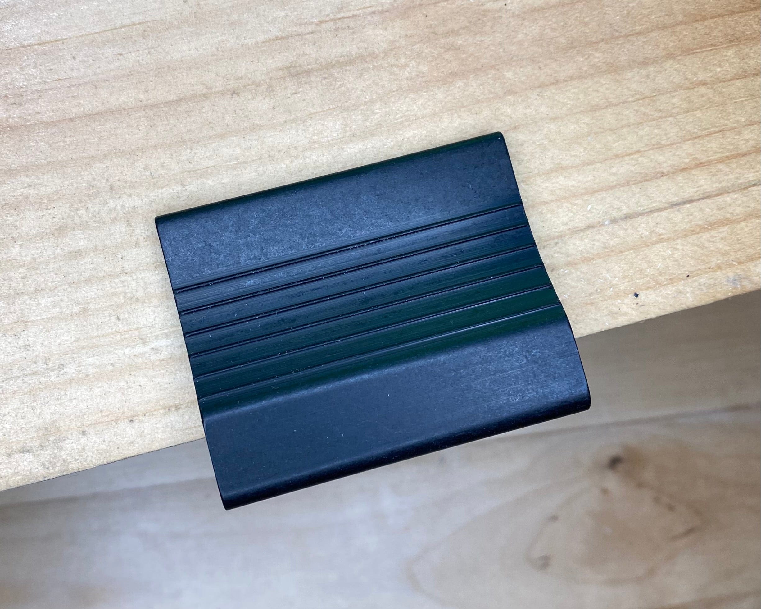 A small, black plastic scraper with grooves rests on a light wooden surface, accompanied by the VERITAS DOVETAIL SADDLE MARKER from VER.