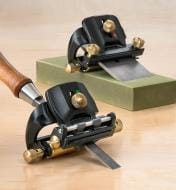 Two MKII DELUXE HONING GUIDE SETs by VER, each holding a chisel, are on a wooden surface—one atop a green sharpening stone and the other on the table—ensuring precise blade angle control for sharpening chisels and plane blades.