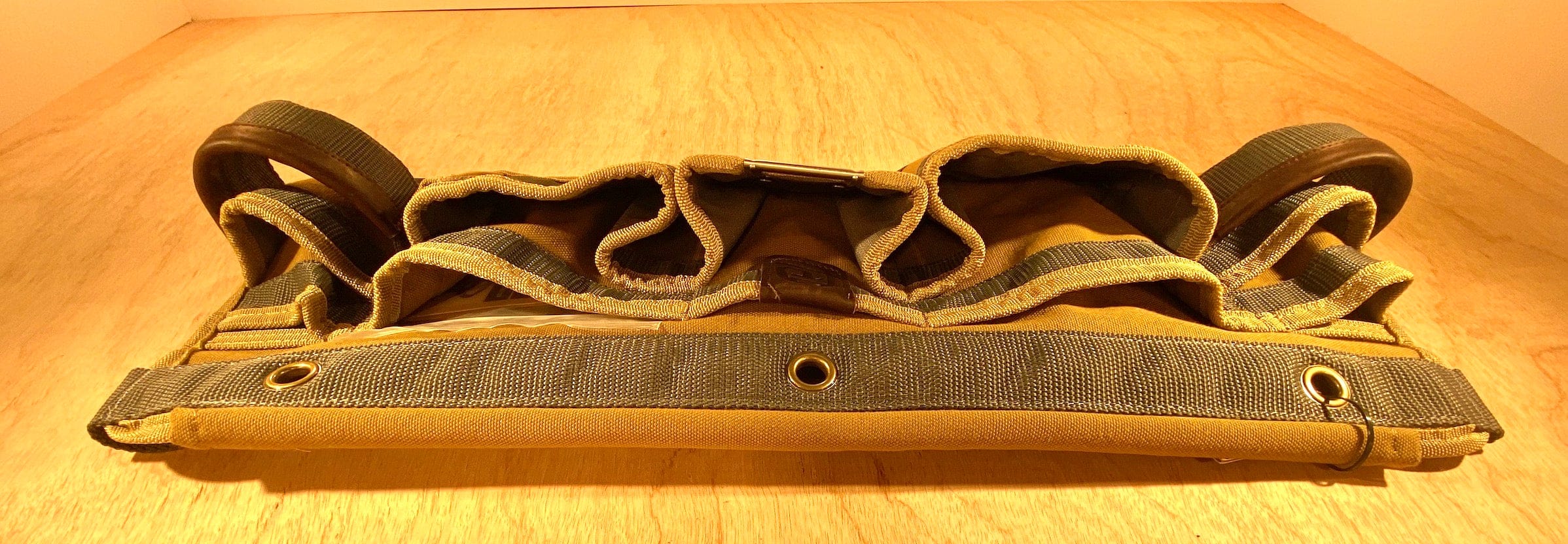 The Veto Pro Pac TA-WB Waist Apron by VET, featuring a brown and green design with an adjustable waist size, multiple pockets, and loops, lies flat on a wooden surface, providing an organized tool storage solution.