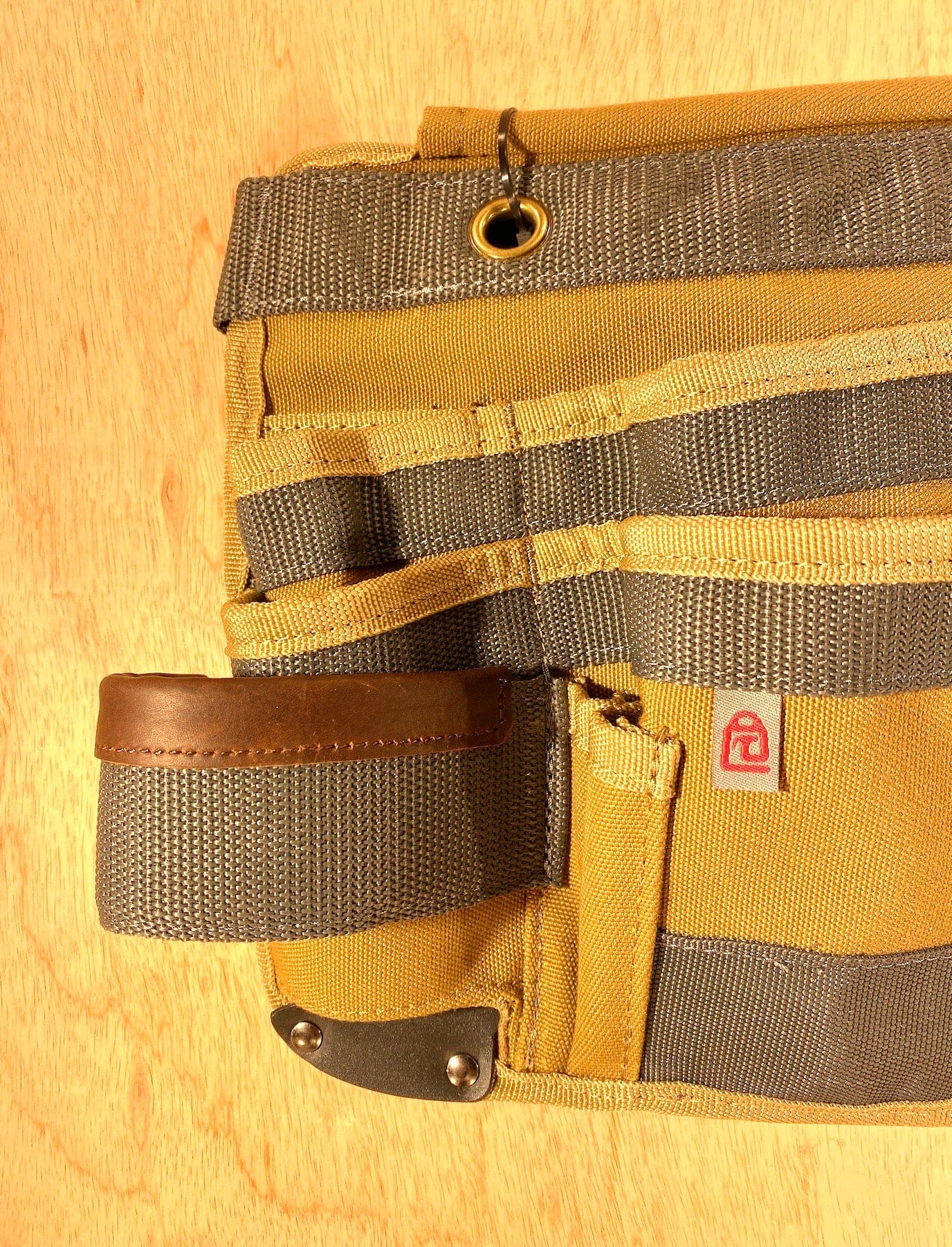 A close-up of the Veto Pro Pac TA-WB Waist Apron by VET, showcasing its tan and gray design with an adjustable waist size, multiple pockets, and a leather loop, laid flat on a wooden surface.