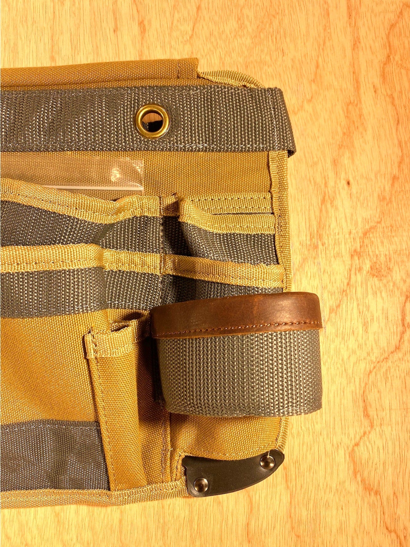 The Veto Pro Pac TA-WB Waist Apron by VET is a versatile tool carrying solution. It features an adjustable waist size with multiple pockets and a loop for hanging, crafted from tan and gray fabric with leather accents. This apron is displayed on a wooden surface for an organized tool storage experience.