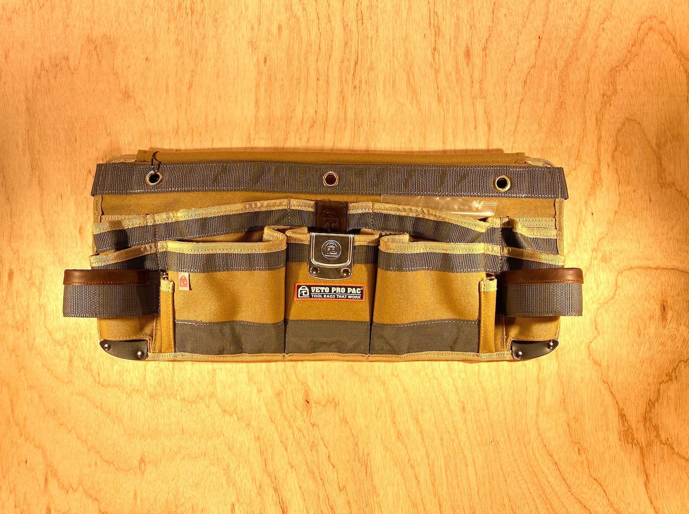 The Veto Pro Pac TA-WB Waist Apron by VET presents a tan tool-carrying solution with an adjustable waist size, offering multiple pockets and a central logo tag, all elegantly arranged on a wooden surface for organized tool storage.