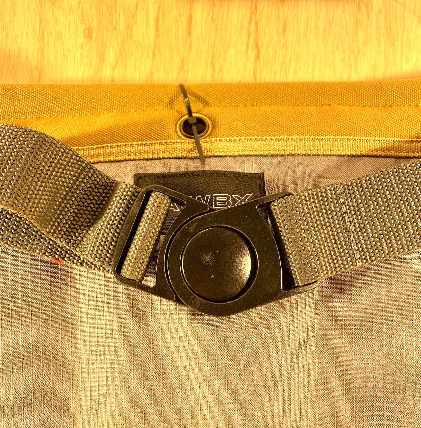 Close-up of a gray strap with a black plastic buckle attached to the yellow fabric of the VET Veto Pro Pac TA-WBX Waist Apron With Boxed Pockets, made from durable polyester canvas and featuring a small black loop and tag.