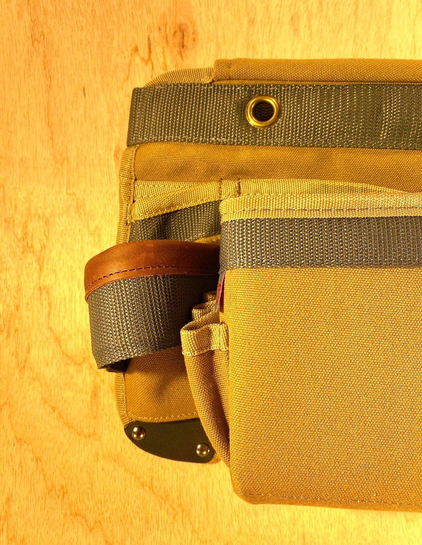 The VET Veto Pro Pac TA-WBX Waist Apron With Boxed Pockets, displayed against a wooden surface, showcases multiple pockets and a brown leather loop in tan and olive green. Made from durable polyester canvas, this tool belt offers excellent storage and functionality.