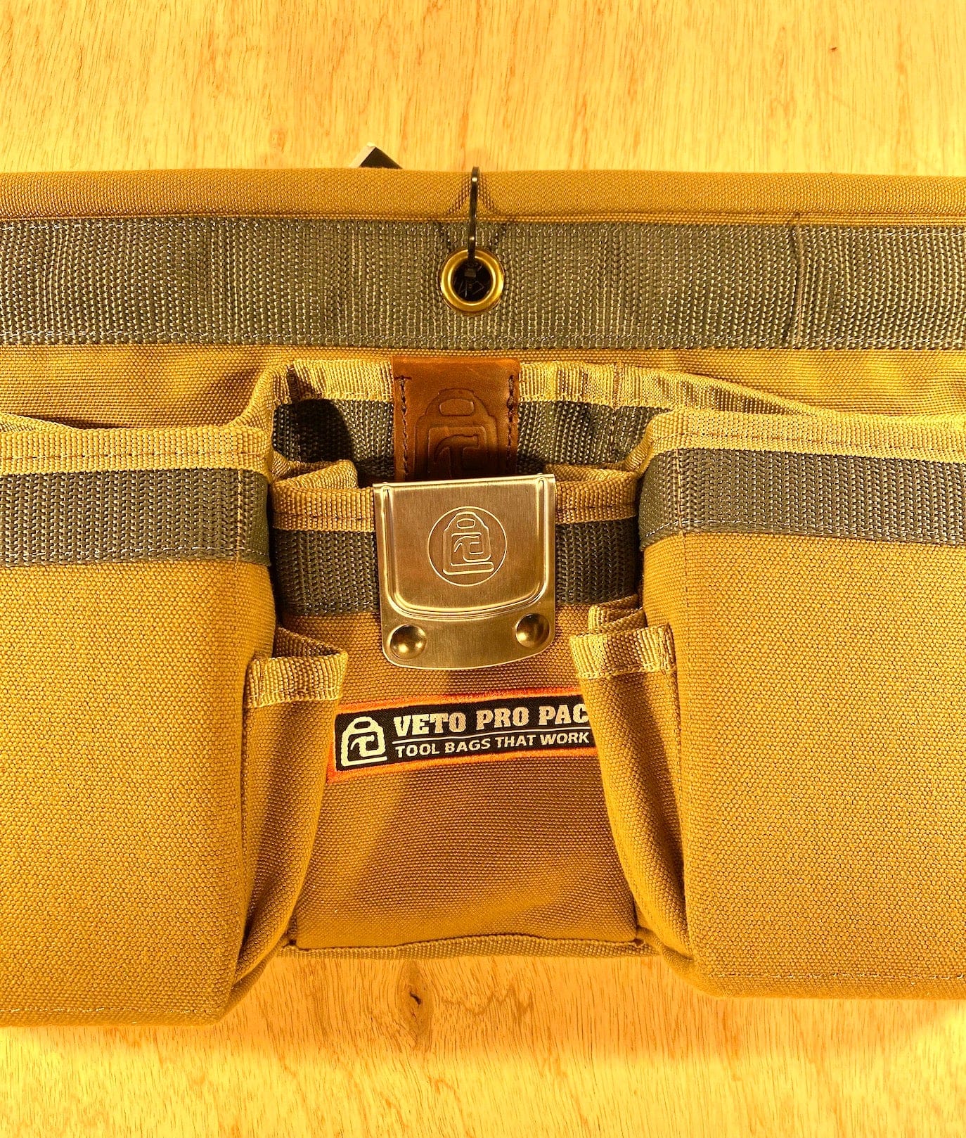 Close-up of the VET Veto Pro Pac TA-WBX Waist Apron With Boxed Pockets, made from durable polyester canvas and featuring multiple pockets and a central metal clasp, on a light wooden surface.