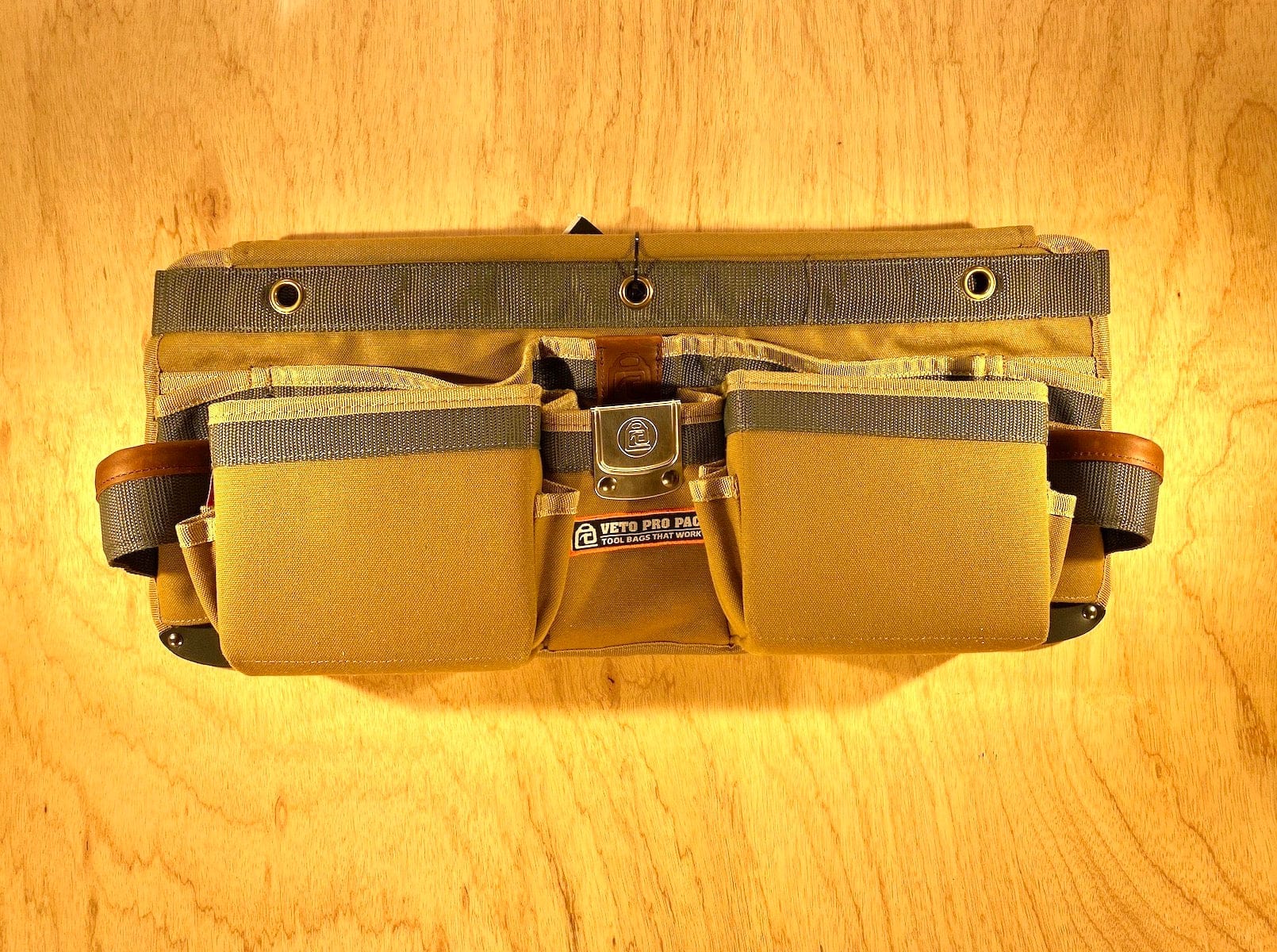A VET Veto Pro Pac TA-WBX Waist Apron with boxed pockets, made from durable tan polyester canvas and featuring multiple compartments and pockets, lying on a wooden surface.